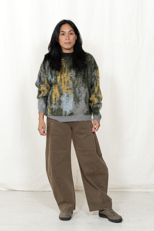 Person wearing a patterned sweater and brown pants on a white background